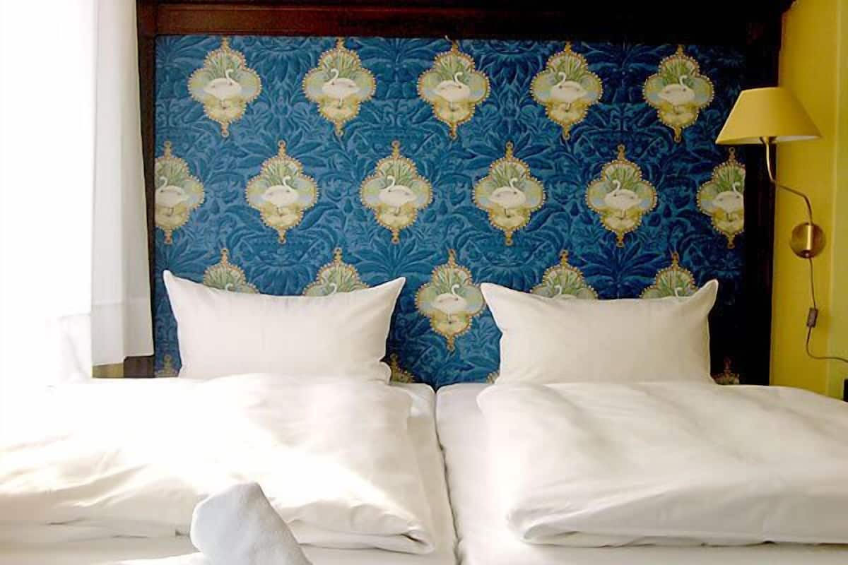 A double bed with white linens in a room with a blue patterned headboard and a yellow wall.