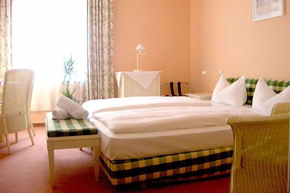 A hotel room with a bed, a chair, a small table, and a window with curtains.