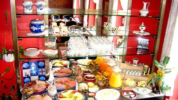 Ein Buffet mit verschiedenen Speisen, darunter Fleisch, Salate und Getränke, präsentiert auf einer Glasplatte vor roten Wänden und dekorativen Elementen im Hintergrund.