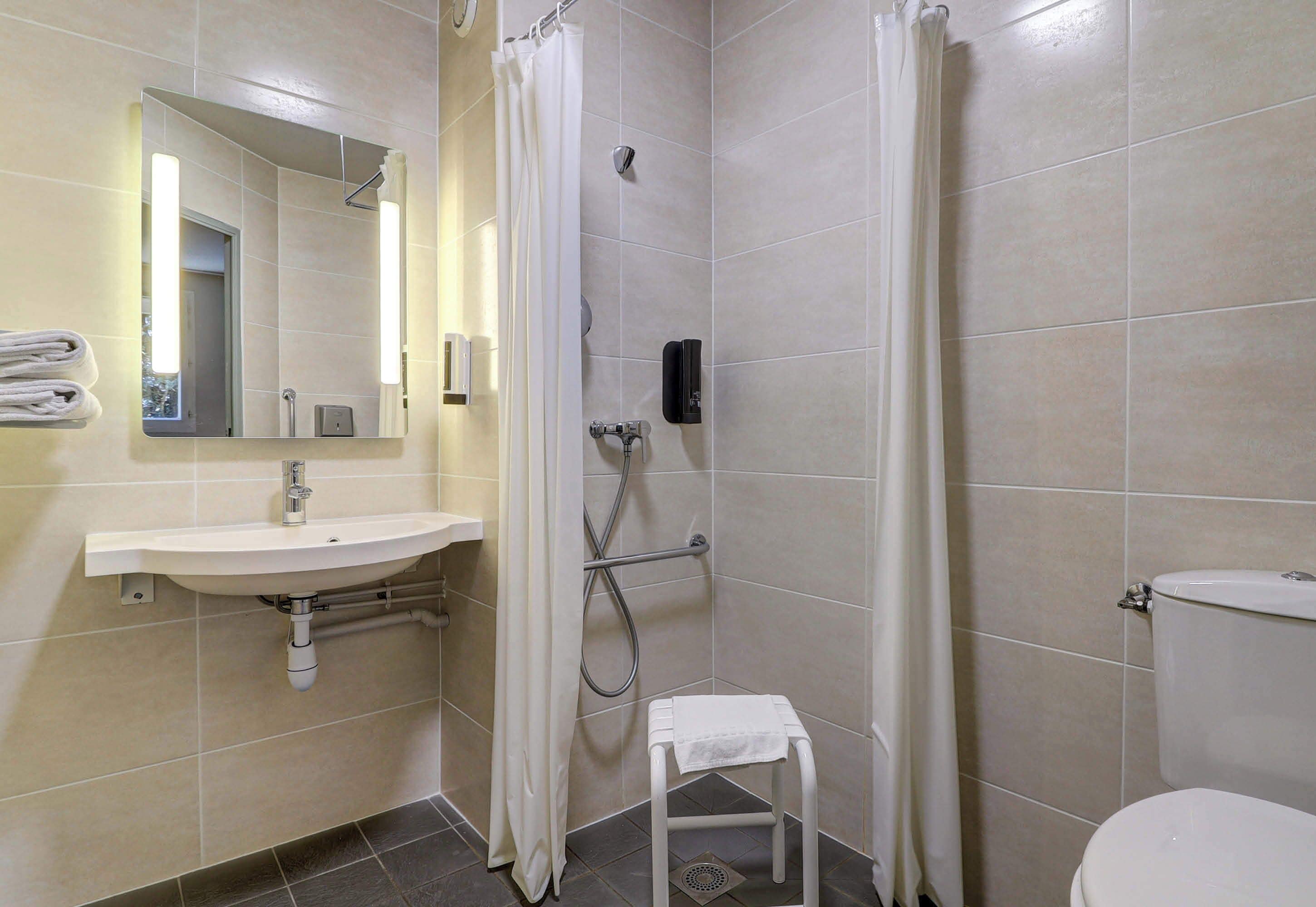 A bathroom with a sink, mirror, shower, toilet, and a small stool.