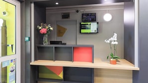 Een receptiebalie met een flatscreenmonitor, een vaas met bloemen en een potplant.