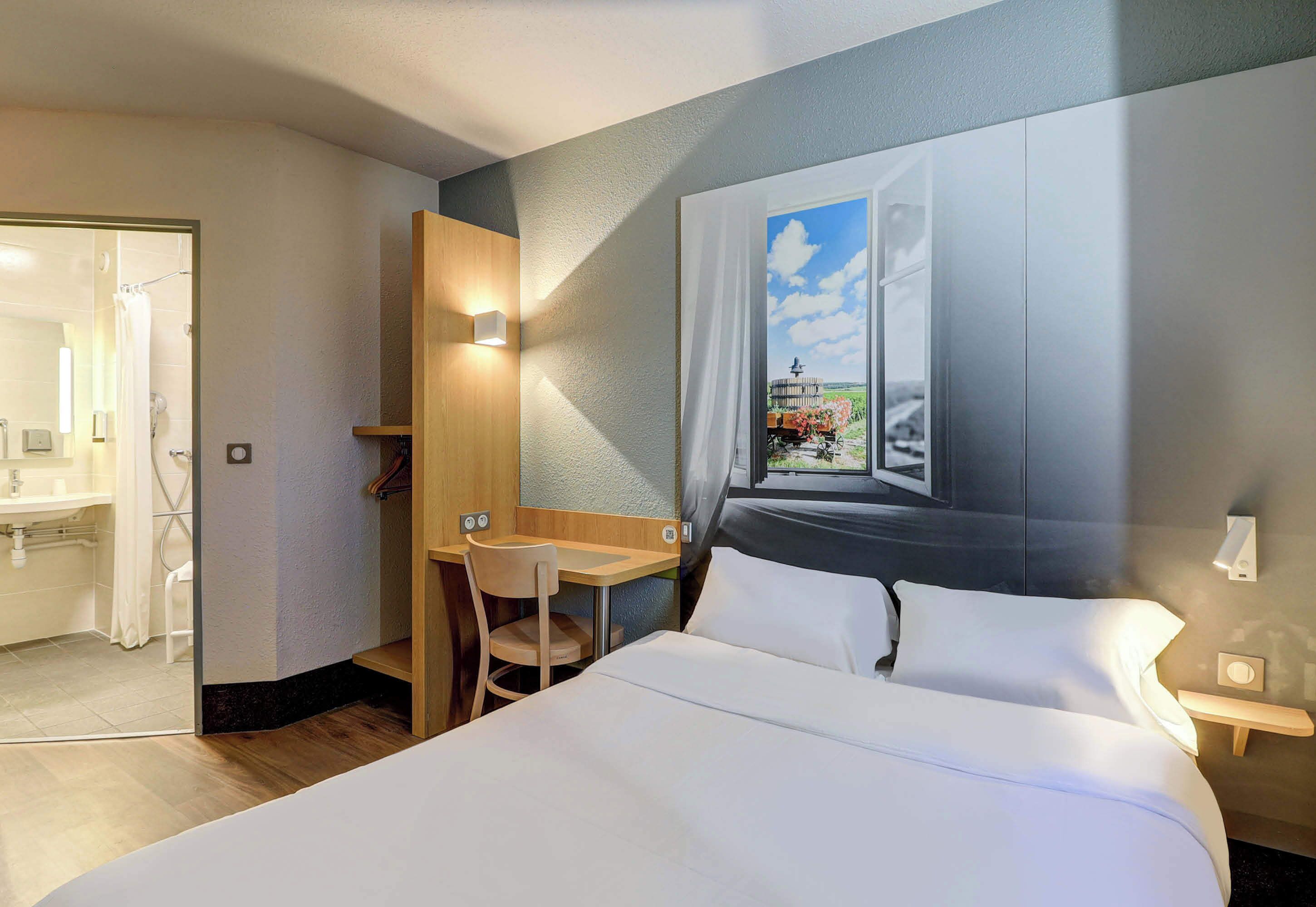 Habitación de hotel con cama, escritorio, silla y un amplio ventanal con vistas al paisaje.