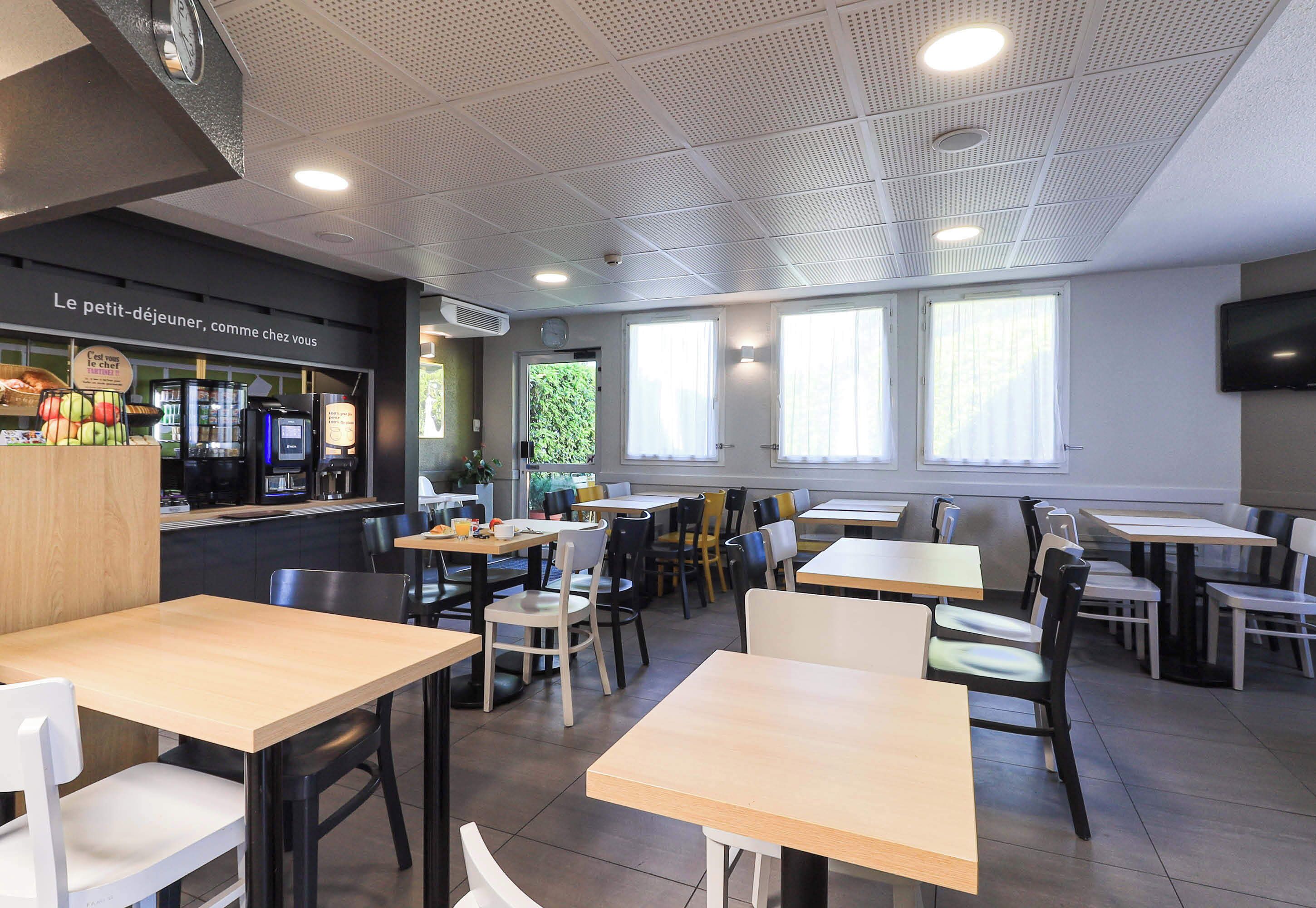 A modern cafe with multiple tables and chairs, a counter with a menu, and large windows allowing natural light.