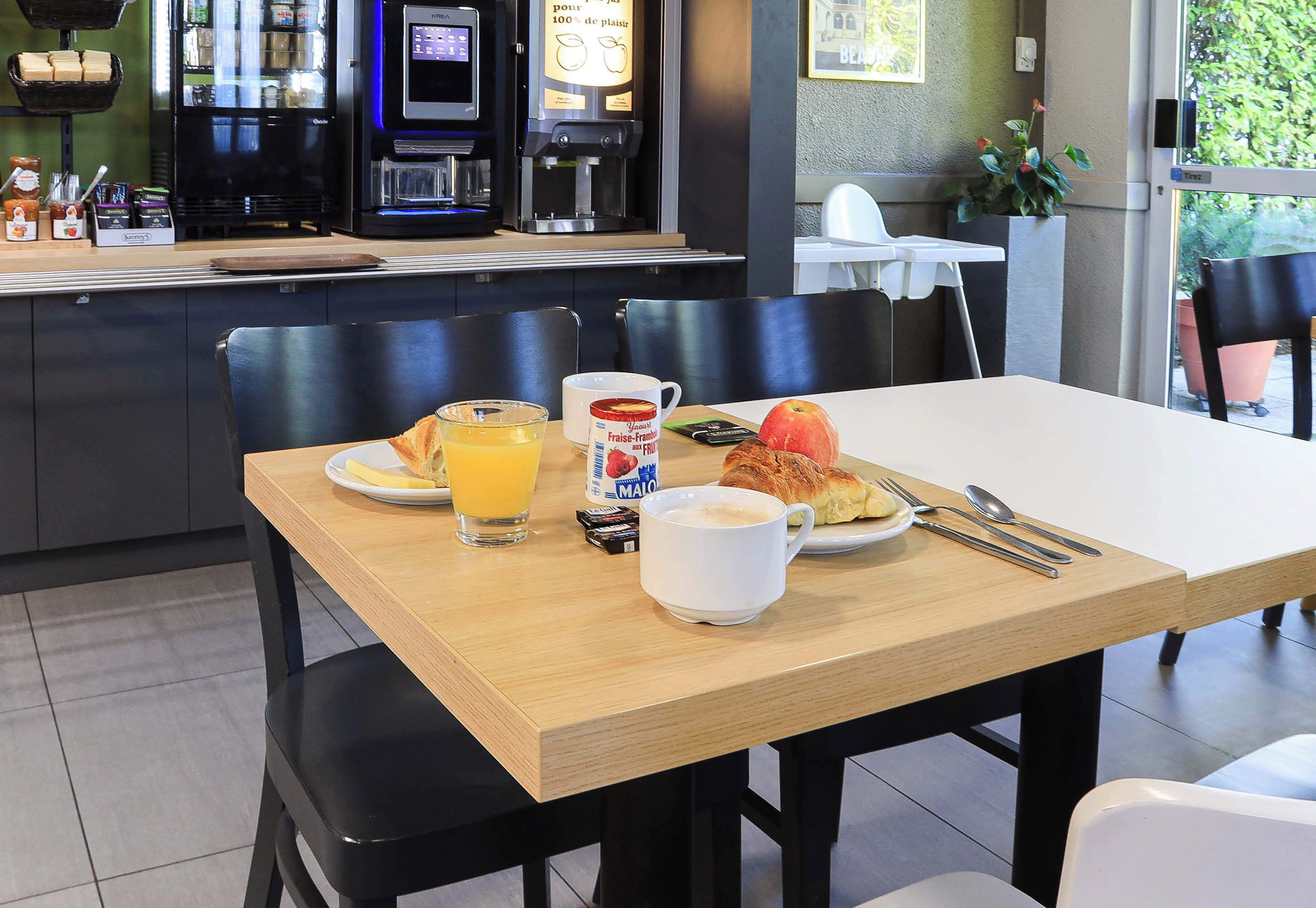 Una mesa de desayuno con un croissant, jugo de naranja, una taza de café y un plato de comida.