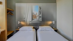 Een hotelkamer met twee bedden, een groot raam en uitzicht op een gebouw.