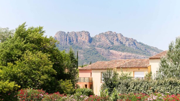 A residential area with a mountain in the background, houses with tiled roofs, and a variety of trees and flowering plants. - B&B HOTEL Fréjus Roquebrune-sur-Argens (Roquebrune-sur-Argens)
