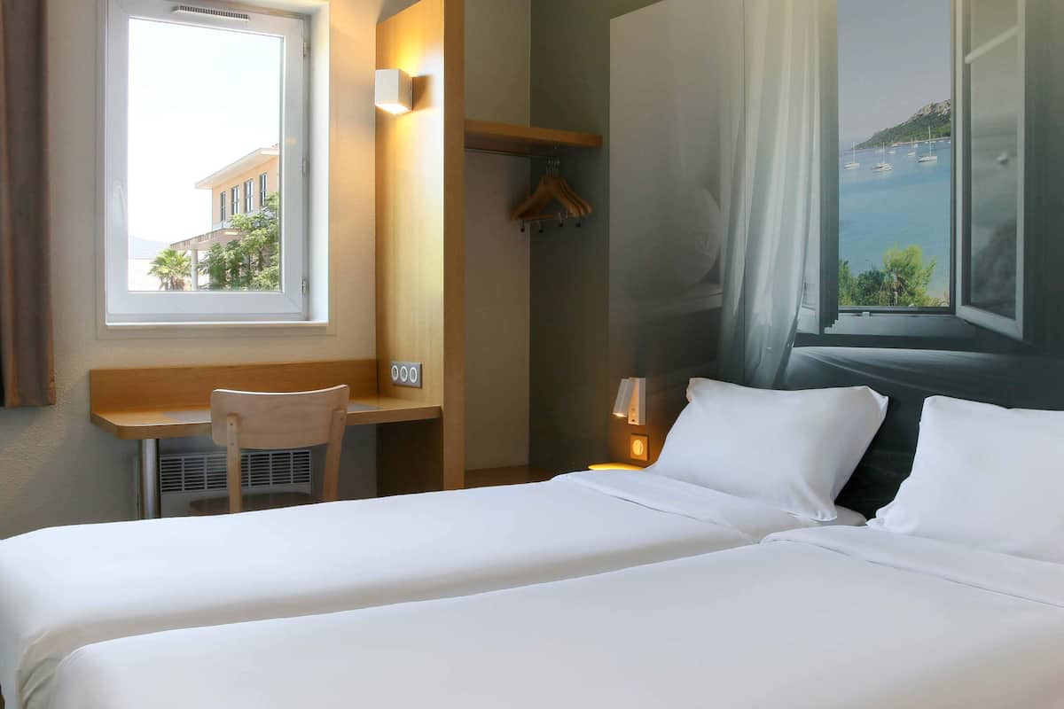 Une chambre d’hôtel avec un lit, un bureau, une chaise, un porte-manteau et une vue sur la mer.