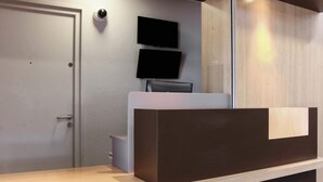 A reception desk with a flat-screen TV, a door, and a wooden panel wall. - B&B HOTEL Fréjus Roquebrune-sur-Argens (Roquebrune-sur-Argens)