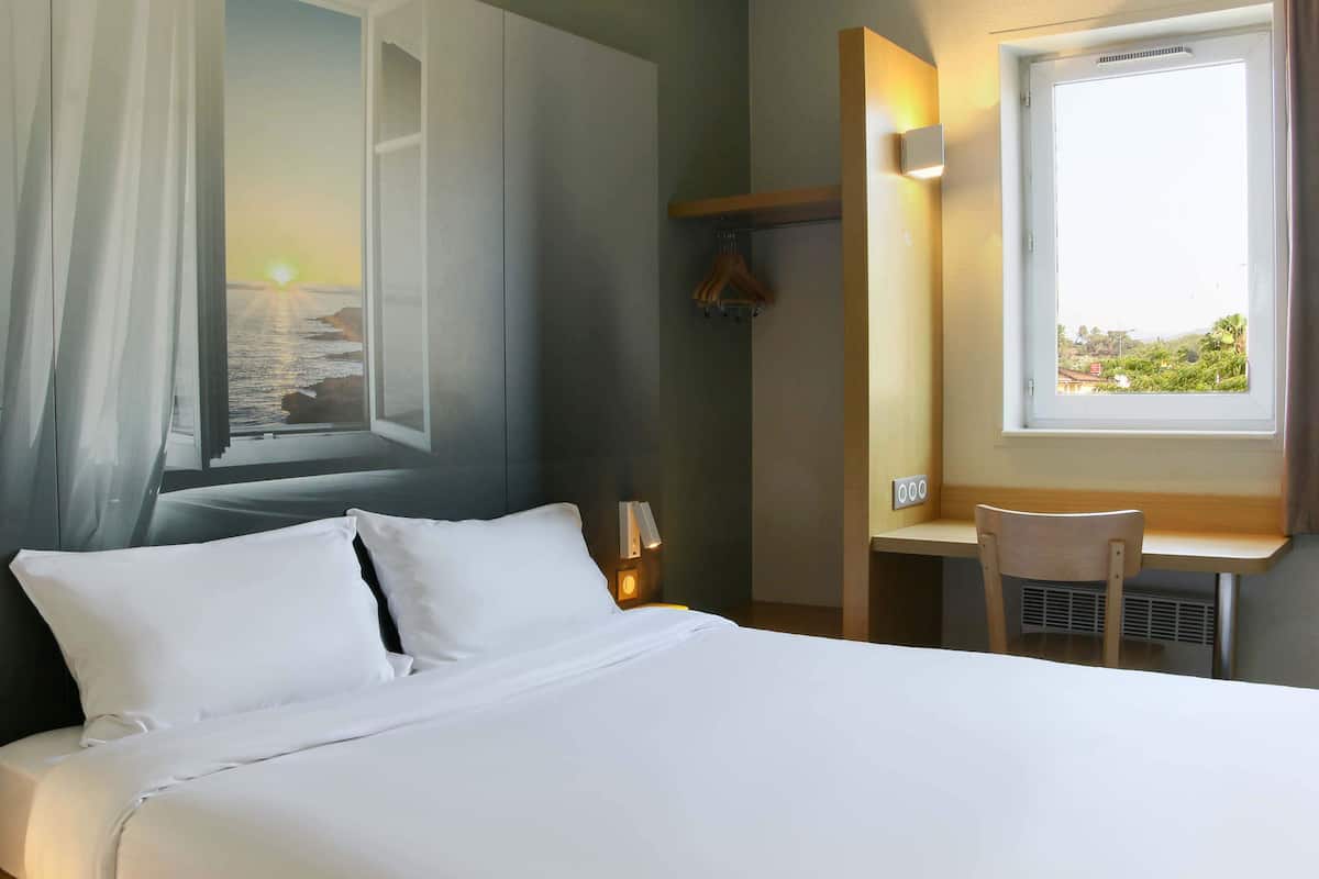 Hotellihuone, jossa on sänky, työpöytä, tuoli, ikkuna, josta on näkymä merelle, ja seinälle kiinnitetty naulakko.