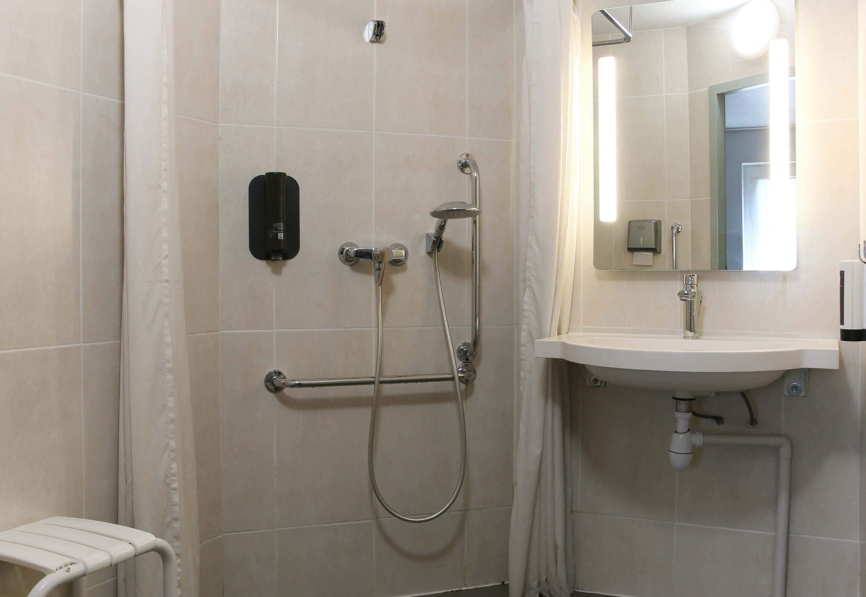 Ein Badezimmer mit Dusche, Handlauf, Waschbecken und Spiegel.