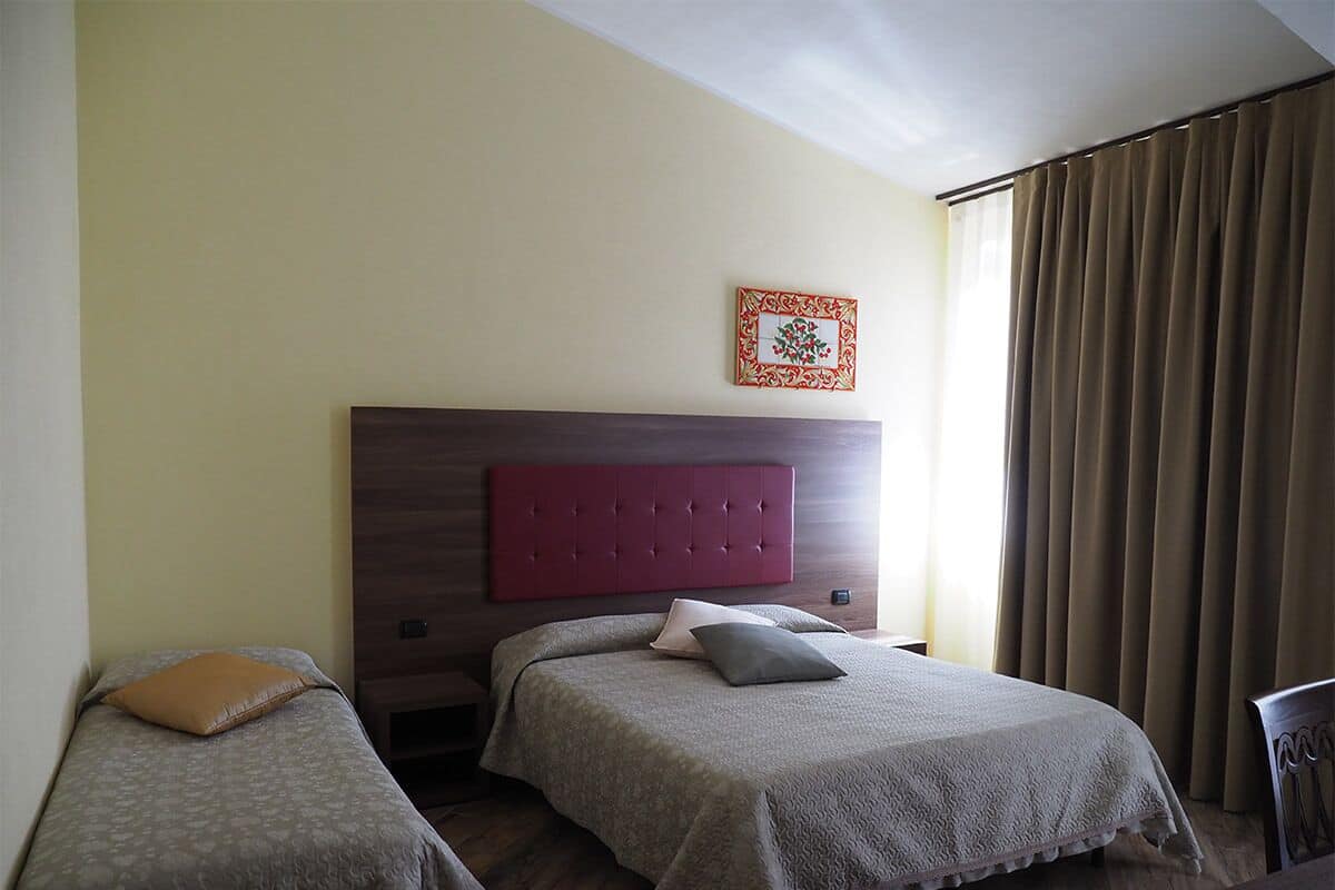 Une chambre d’hôtel avec deux lits simples, une tête de lit en bois, un élément décoratif mural et une fenêtre avec des rideaux.