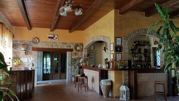 Un interior espacioso con techo de madera, paredes de piedra, una zona de bar con botellas y una planta grande en maceta.