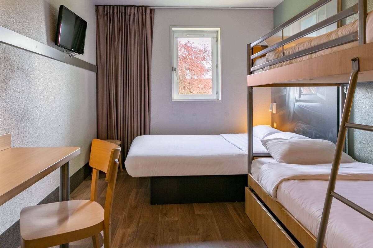 Une petite pièce avec des lits superposés, un bureau, une chaise et un téléviseur fixé au mur.