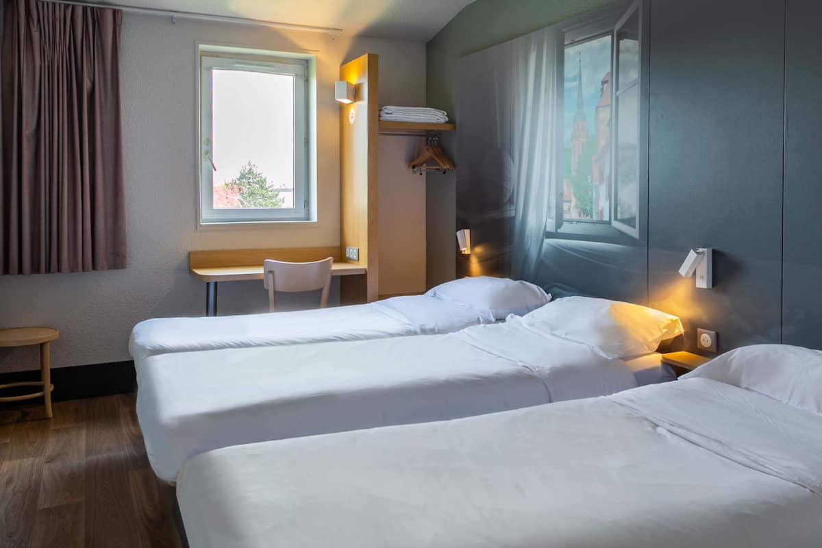 Une chambre d’hôtel avec deux lits simples, un bureau, une chaise et une fenêtre avec des rideaux.