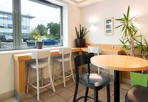 Eine moderne Bar mit einer Holztresen, weißen und schwarzen Barhocker und Topfpflanzen.