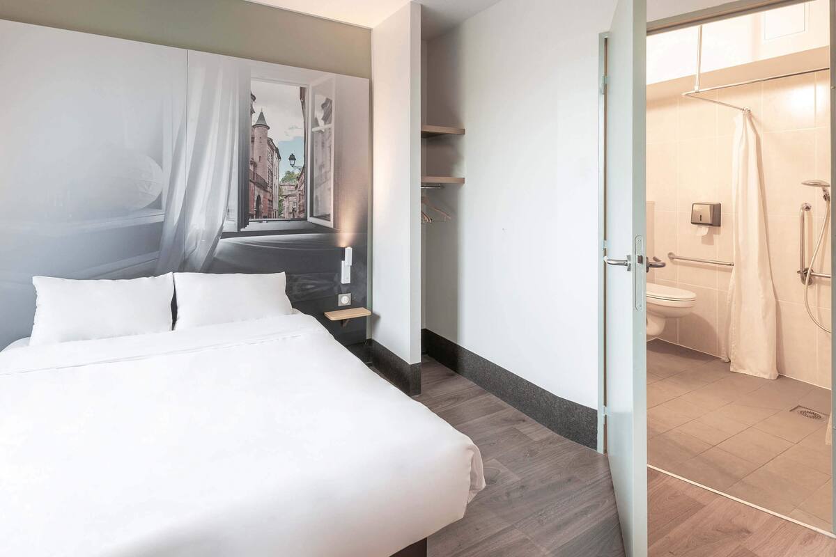 Habitación de hotel con cama, ducha y vista a la calle a través de una ventana.