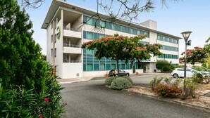 A modern building with a flat roof, large windows, and a parking area with cars. - B&B HOTEL Toulouse Basso Cambo (Toulouse)