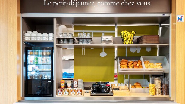 A breakfast counter with a refrigerator, bowls, cups, and pastries. - B&B HOTEL Toulouse Basso Cambo (Toulouse)
