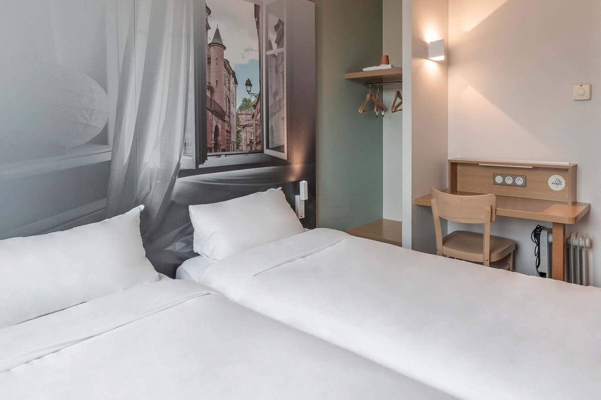 Habitación de hotel con cama, escritorio y estante de pared con perchas.