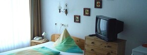 Habitación de hotel con una cama, una mesita de noche de madera, un televisor y una pared decorada con cuadros.