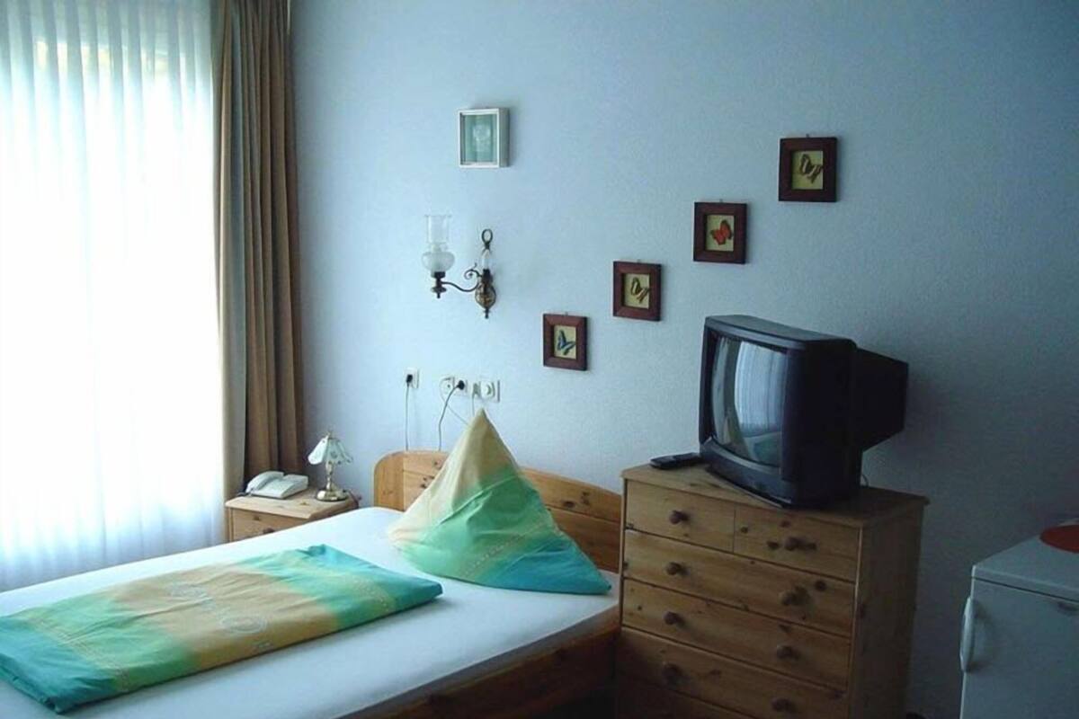 Quarto de hotel com cama, cómoda de madeira, televisão e janela com cortinas.