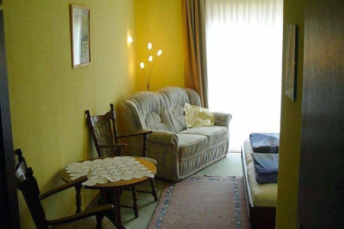 Quarto com sofá, cadeira, mesa pequena com toalha de renda e cama com manta azul.