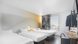 A hotel room with three beds, a desk with a laptop, a suitcase, and a view of the city. - B&B HOTEL Lyon Centre Part-Dieu Gambetta (Lyon)
