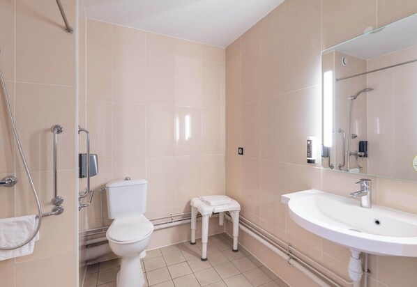 Un baño moderno con inodoro, un taburete pequeño blanco, una cabina de ducha de vidrio y un lavamanos con espejo.