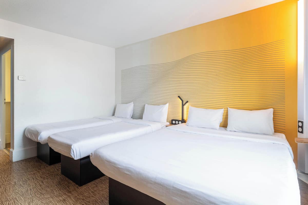 A hotel room with two beds, a modern headboard, and a bedside table with a lamp.