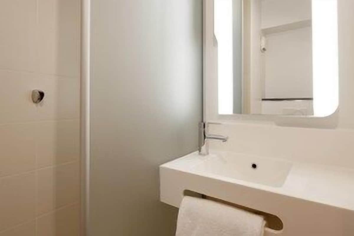 Un baño con lavamanos blanco, un espejo y un perchero para toallas.
