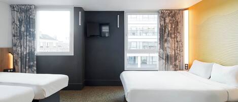Hotelkamer met twee bedden, een flatscreen televisie, een raam met gordijnen en uitzicht op gebouwen.