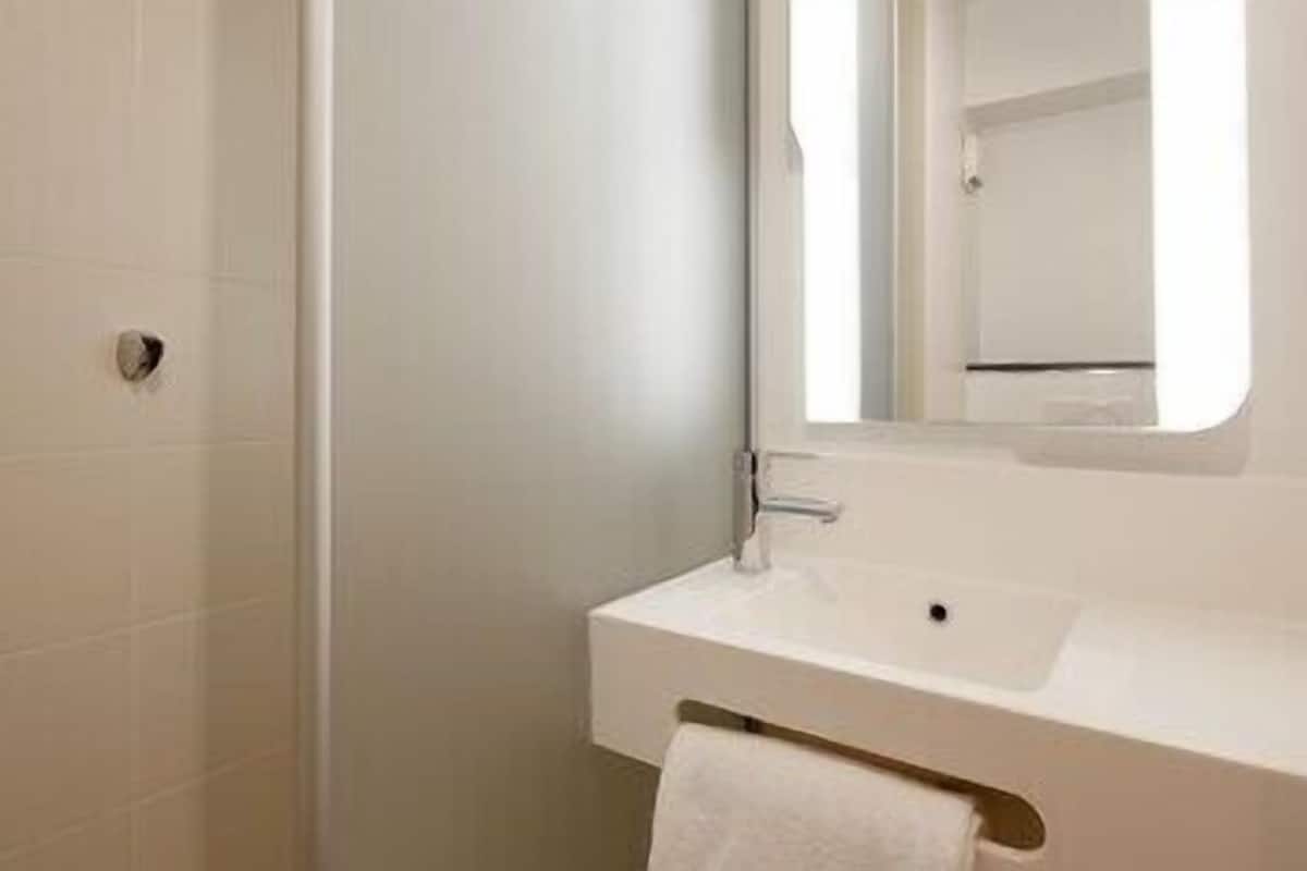 Un baño con lavamanos blanco, un espejo y un perchero para toallas.