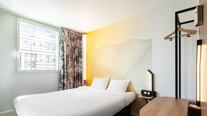 Ein Hotelzimmer mit einem großen Bett, einem Nachttisch, einem Schreibtisch und einem Spiegel.