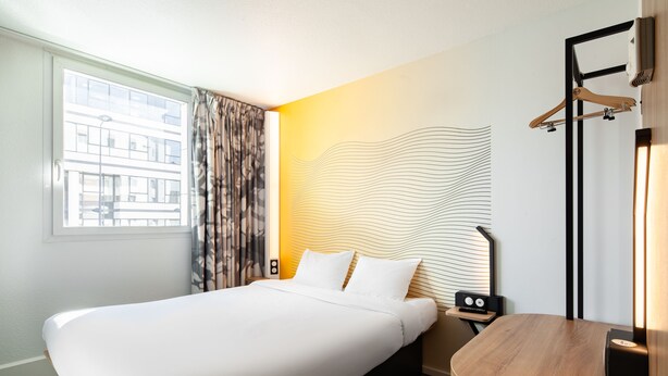 Quarto de hotel com uma cama grande, mesa de cabeceira, escrivaninha e espelho.