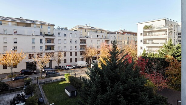 Ein mehrstöckiges Wohngebäude mit Balkonen, einem Parkplatz und einem kleinen Innenhof mit Bäumen und Sitzgelegenheiten.