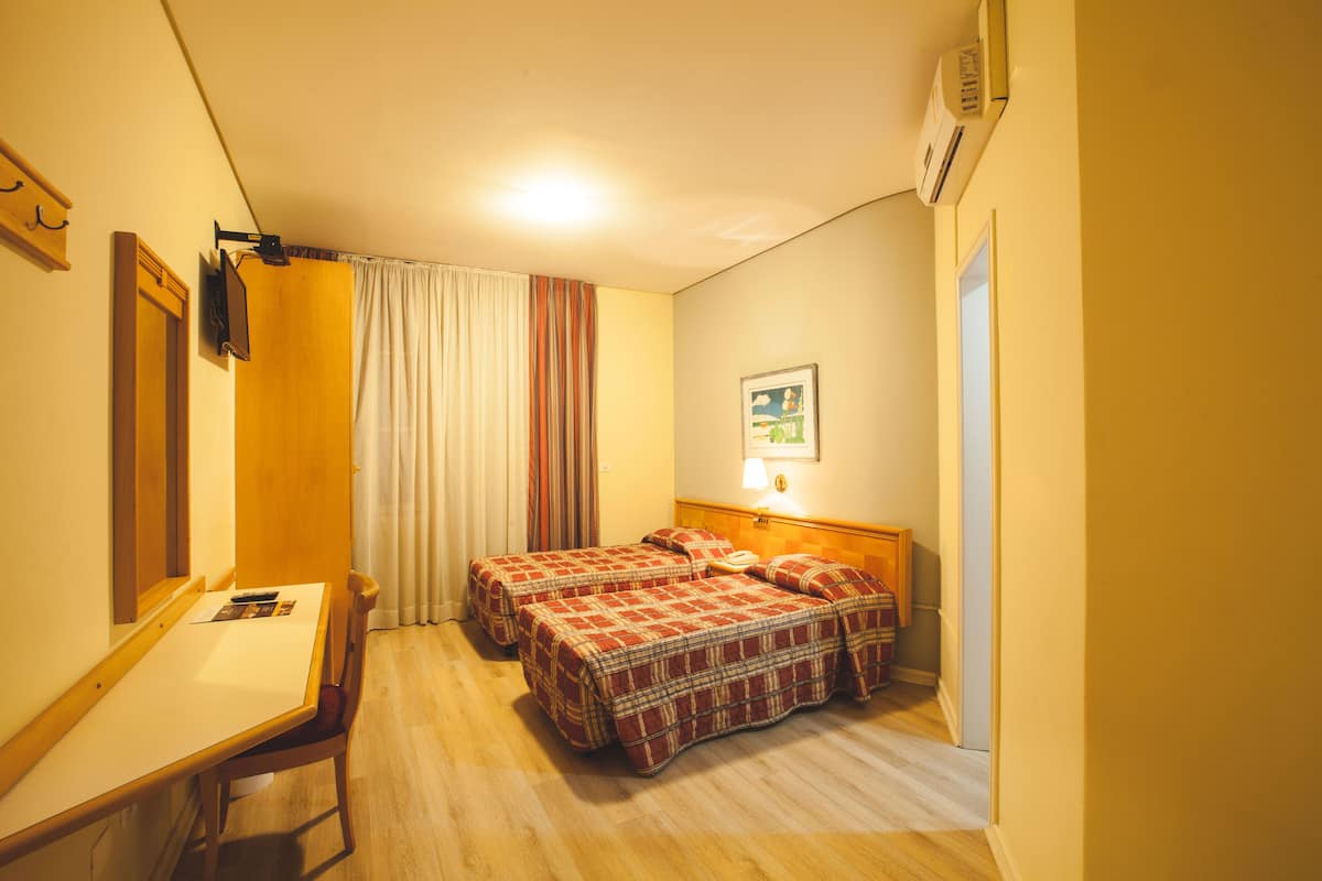 A hotel room with two beds, a desk, a chair, a TV, and a picture on the wall.