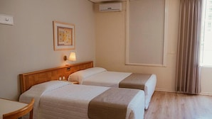Ein Hotelzimmer mit zwei Betten, einem Holzkopfteil, einem Nachttisch, einer Lampe und einem Fenster mit Vorhängen.