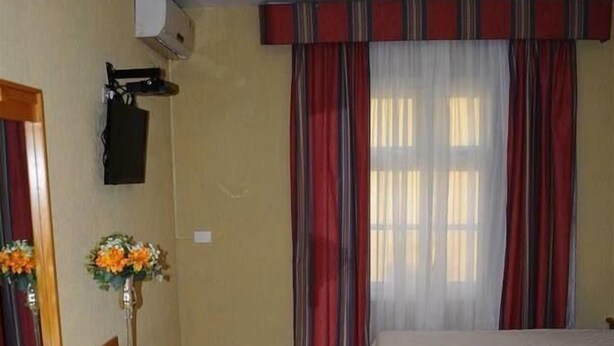 A hotel room with a bed, a desk with a chair, a mirror, and a window with curtains. - Curitiba Palace Estação (Curitiba)