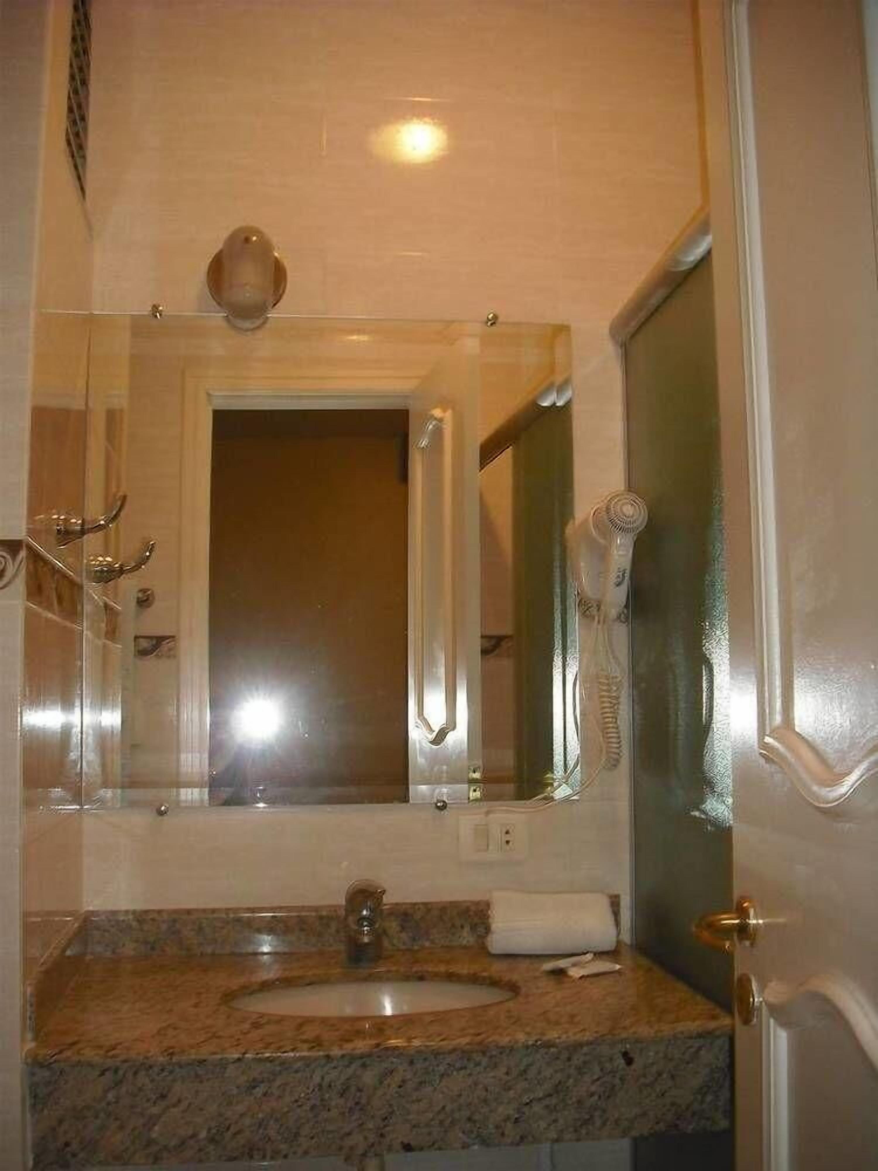 A bathroom with a granite countertop sink, a mirror above it, and a towel rack.