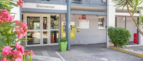 A hotel entrance with a 'Bienvenue' sign, a wheelchair-accessible parking space, and a green planter.