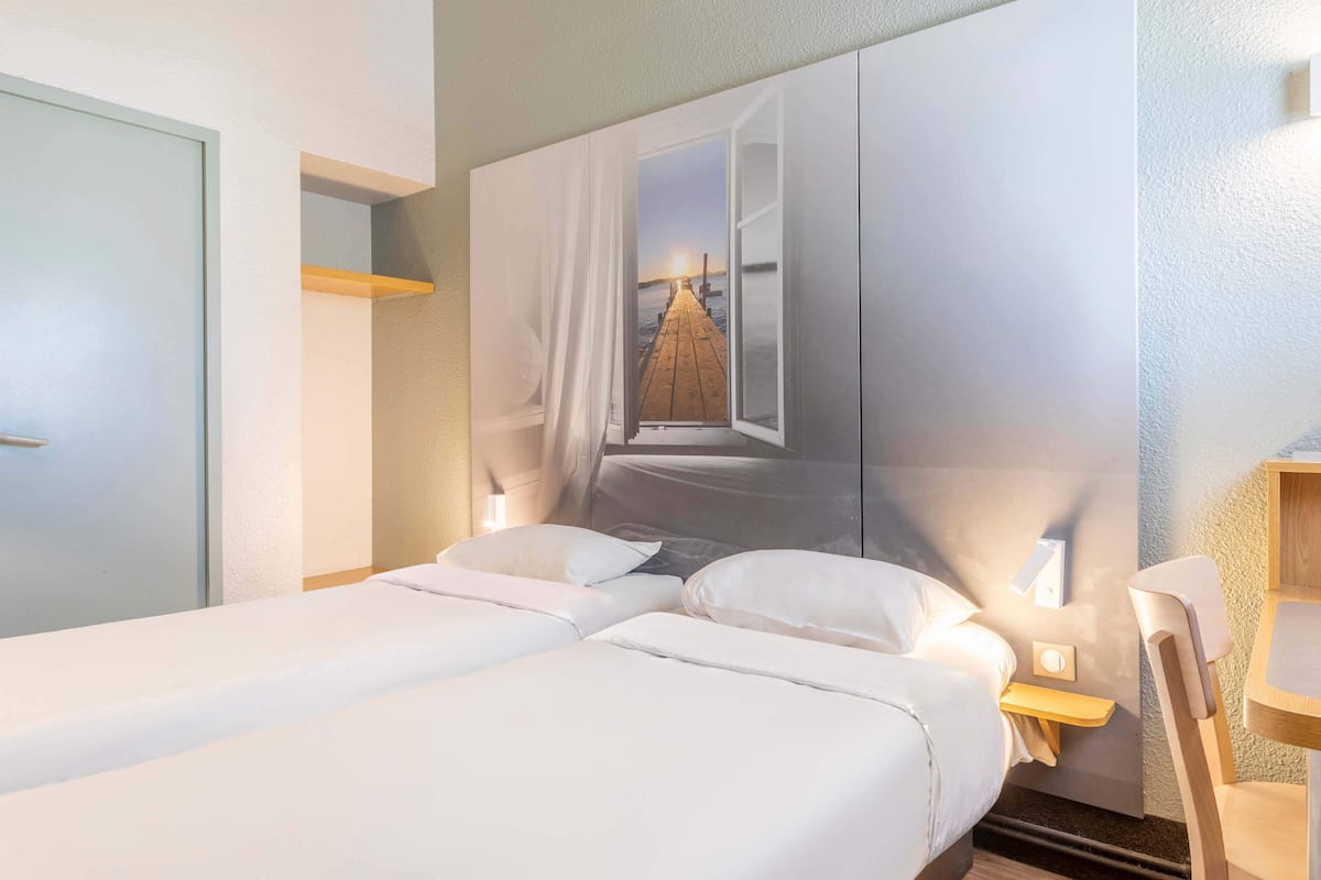 A hotel room with a bed, a nightstand, a chair, and a wall with a large window.