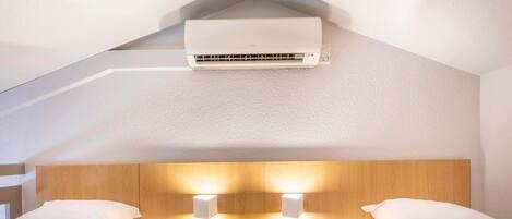 Une chambre d’hôtel avec deux lits, une tête de lit en bois, des lampes fixées au mur et un appareil de climatisation.