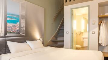 A hotel room with a bed, a view of a cityscape, a staircase, and a bathroom with a towel rack.