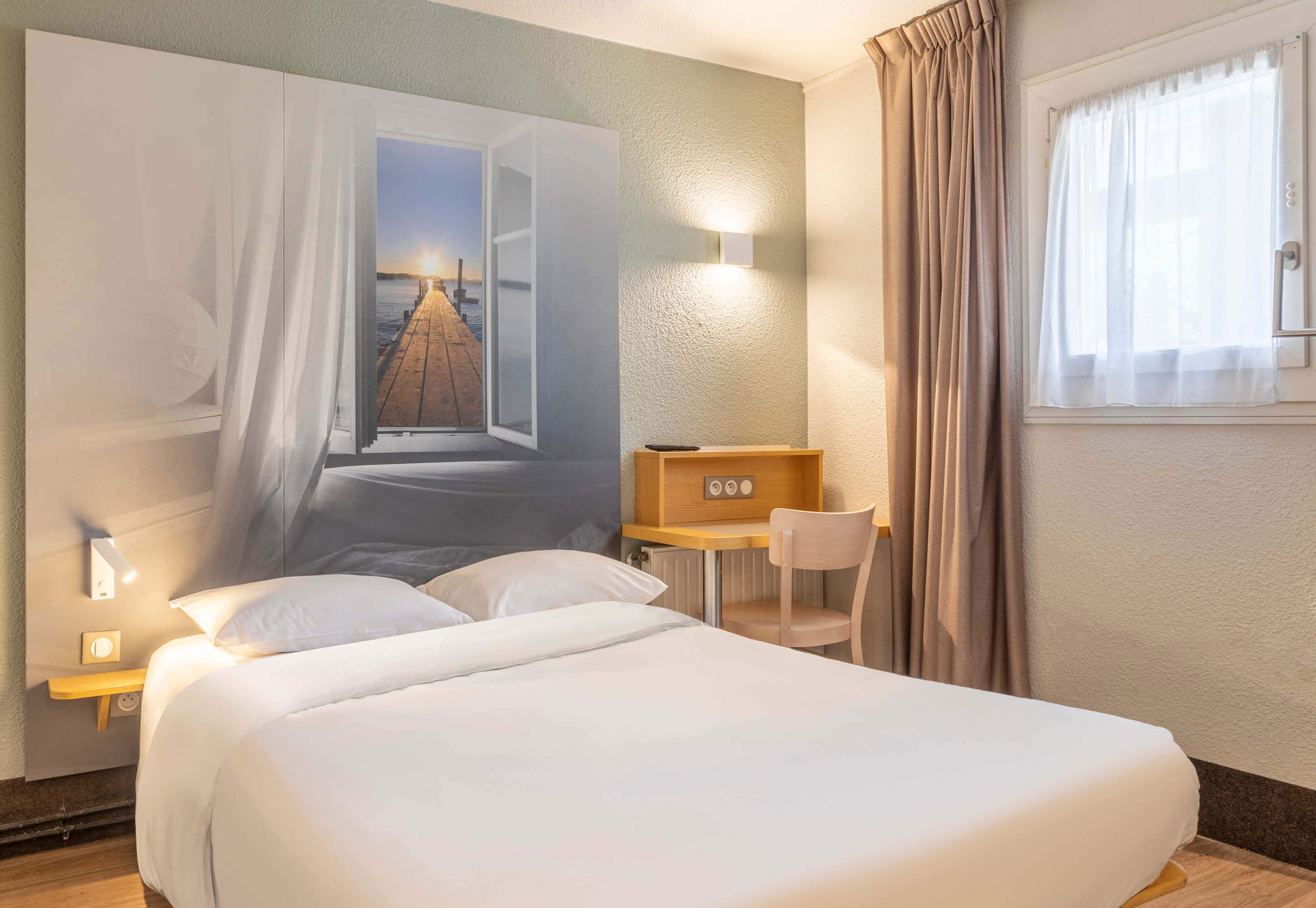 Hotelkamer met een groot bed, een bureau, een stoel en een tv aan de muur.