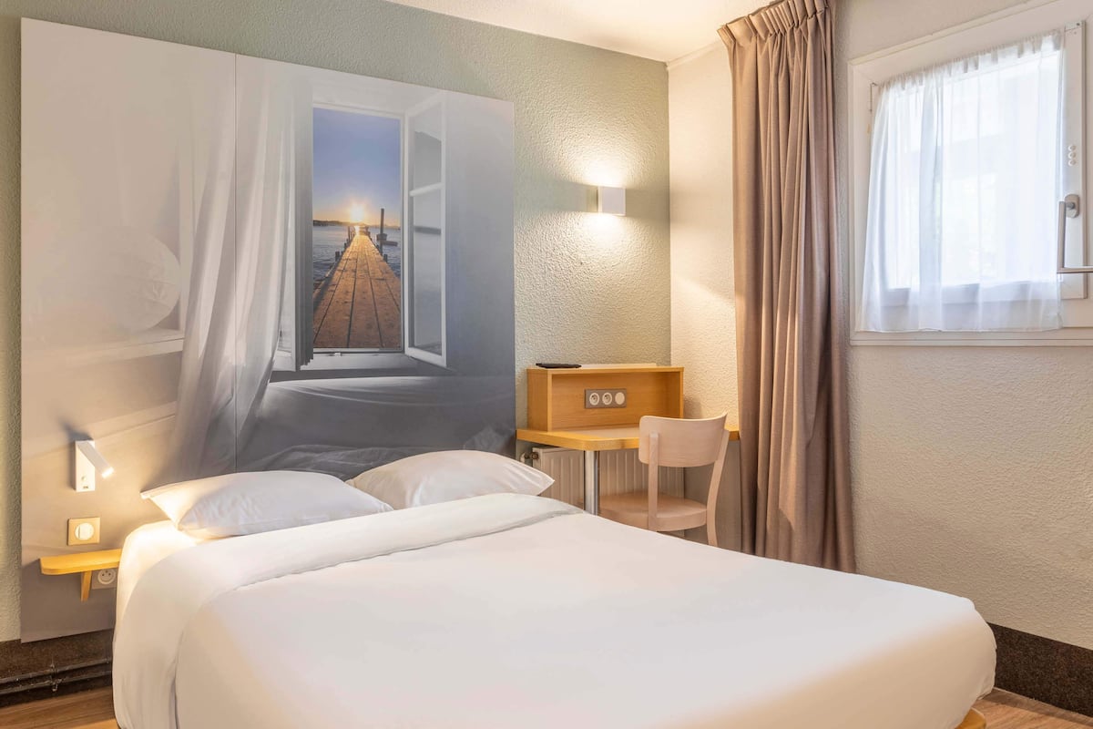 A hotel room with a large bed, a desk, a chair, and a wall-mounted TV.