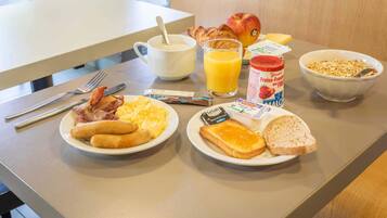 Una mesa de desayuno con platos de huevos, tostadas, cruasanes y un vaso de jugo de naranja.