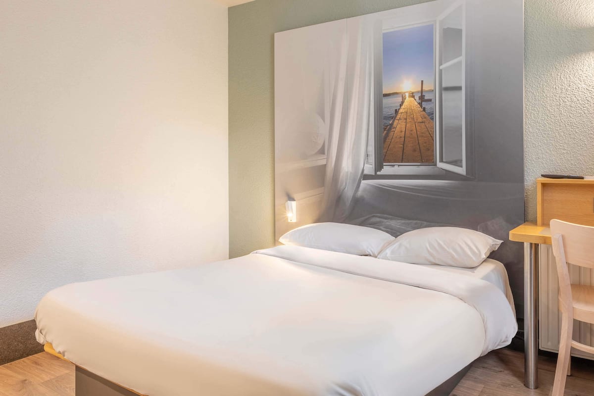 A bedroom with a bed, a nightstand, a chair, and a wall-mounted lamp.
