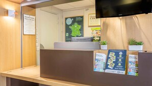 Un espace d’accueil avec un comptoir en bois, un téléviseur à écran plat fixé au-dessus, et des brochures d’information disposées sur le comptoir.