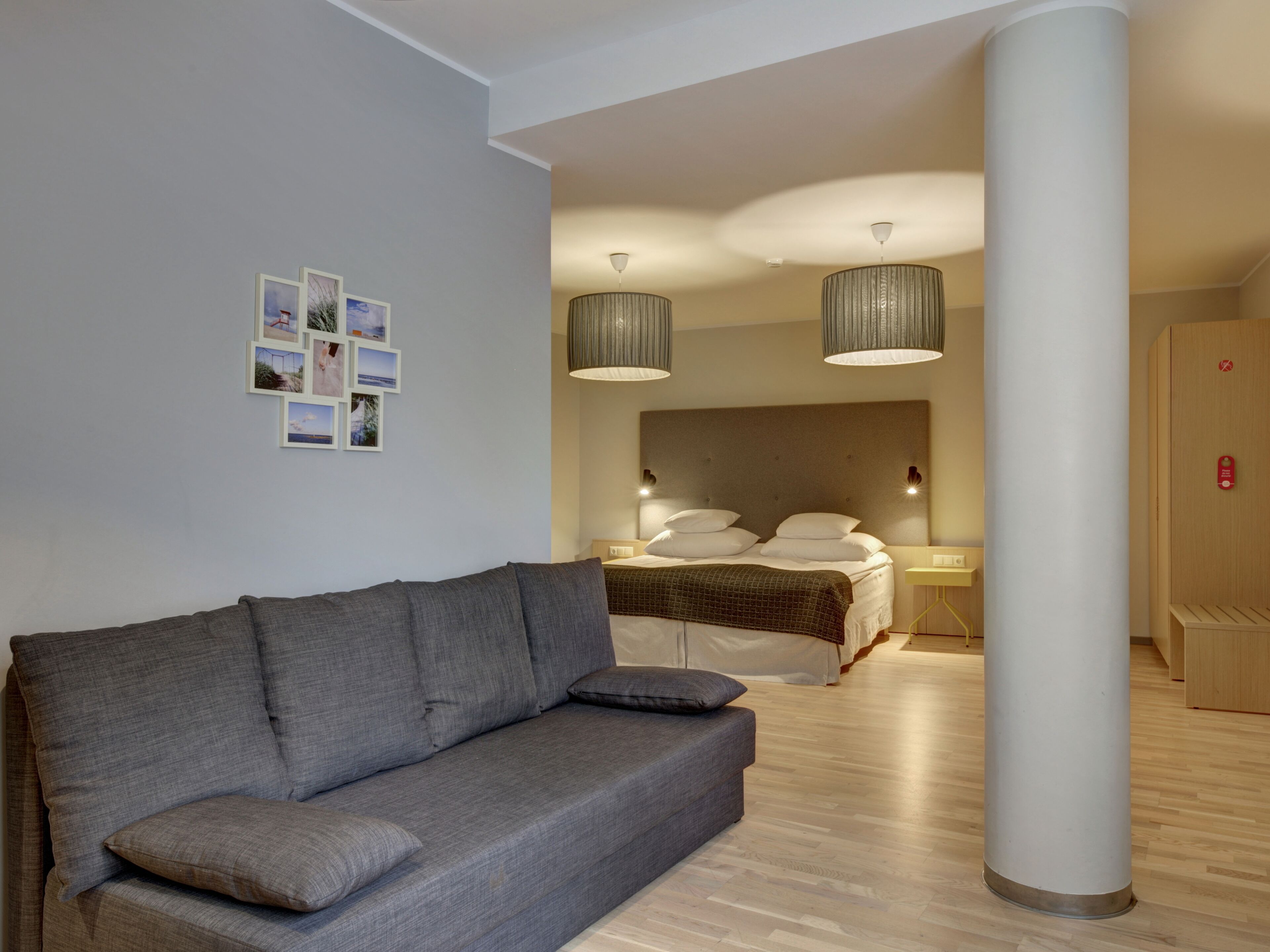 Una habitación de hotel moderna con un sofá gris, una cama con ropa de cama blanca y un armario de madera.