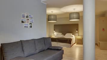 Una habitación de hotel moderna con un sofá gris, una cama con ropa de cama blanca y un armario de madera.